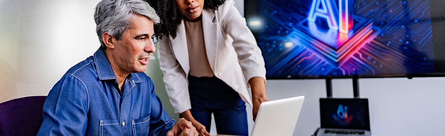 Small Business Team Using AI Technology in Office Two professionals discussing AI strategies for small business on a laptop, with an AI graphic on a screen in the background.